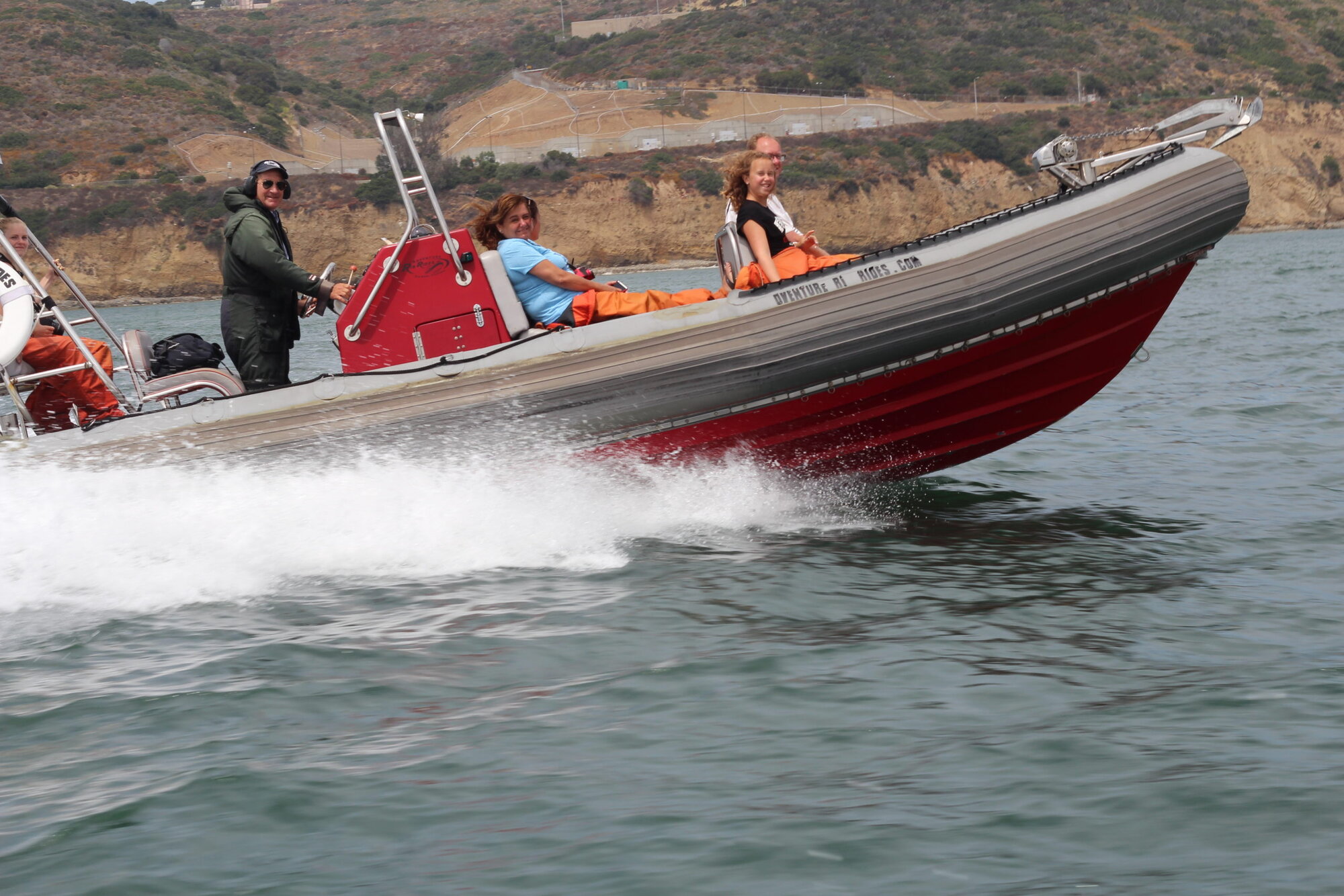 Adventure Whale Watching's red rigid-inflatable boat cutting across the water with guests aboard, San Diego bluffs behind
