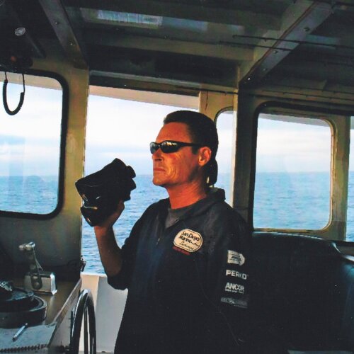 An Adventure Whale Watching captain at the helm, scanning the ocean in branded gear