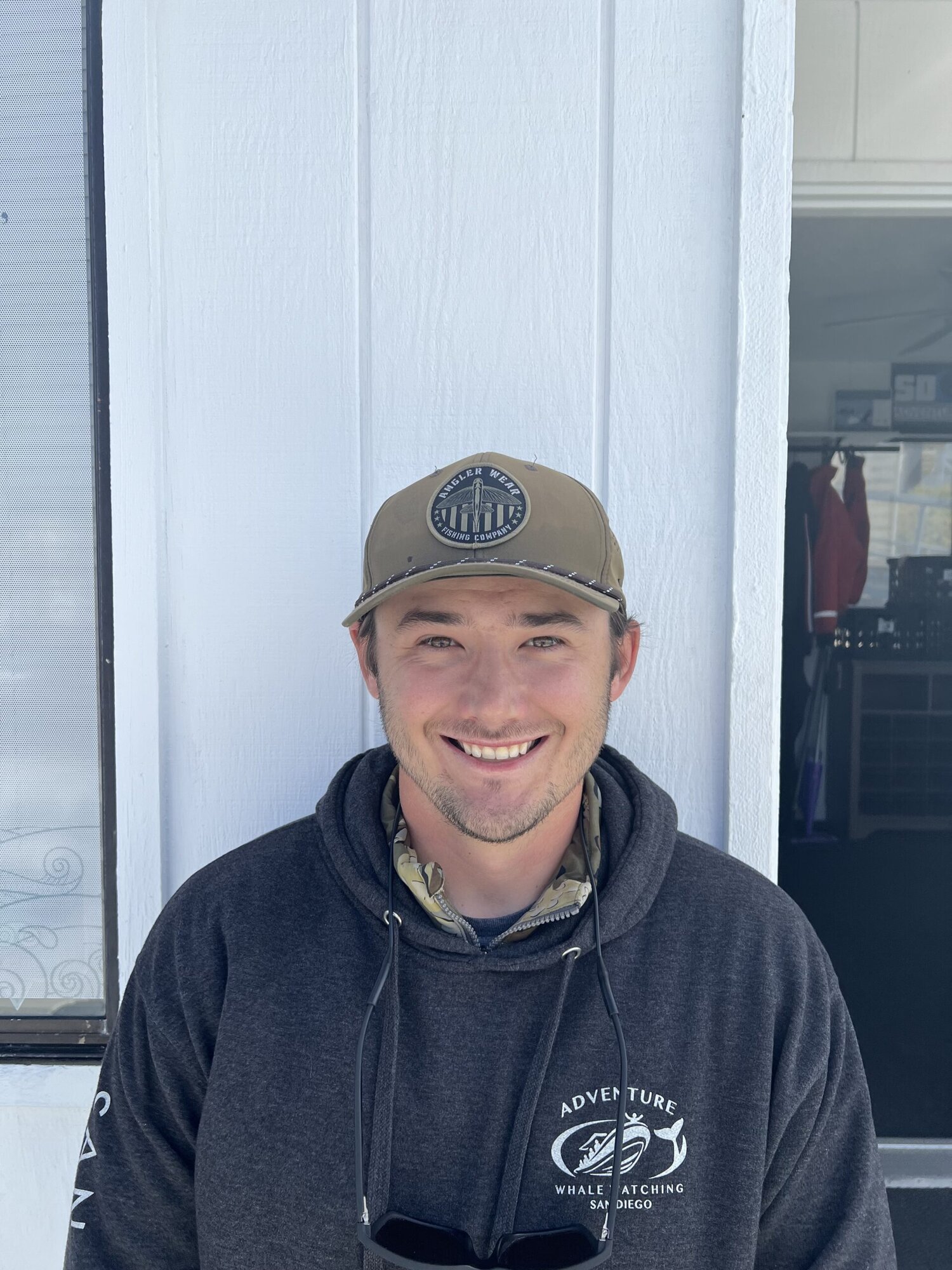 A smiling Adventure Whale Watching crew member in a branded hoodie at the dock office